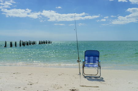 Fishing rod and a chair next to the ocean at summer under the blue skyの写真素材