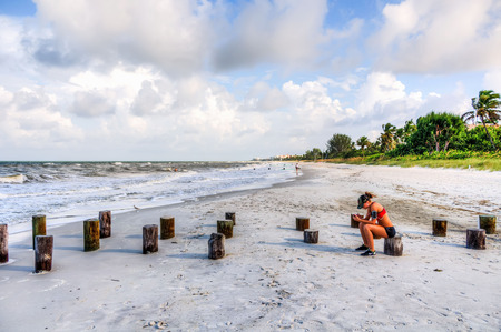 Naples, FL - Sept. 26, 2013: Pretty and athletic girl relaxing and reading phone at the beach after running excerciseのeditorial素材
