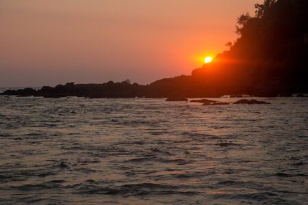 Tropical sunset on rock beach, Goa, Indiaの写真素材