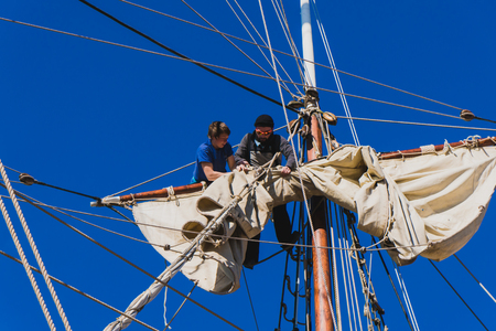 Sailors work with sails at a height on a traditional sailboatの写真素材