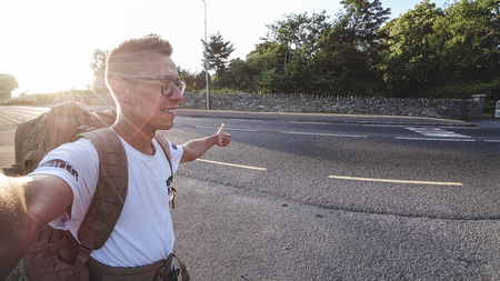 Young man hitchhiking at sunset. View by selfieの写真素材