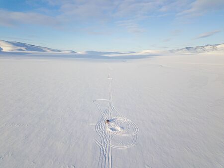 Road leading to nowhere. Aerial photography of a single rut among the snowy desert and mountainsの写真素材