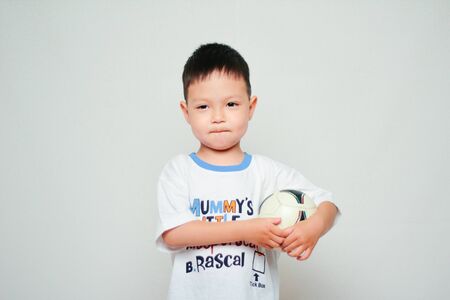 Portrait of Asian four year old boy holding soccer ball on white background, football themeの写真素材