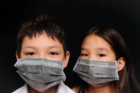Portrait of two Asian kids in medical masks on a black backgroundの写真素材