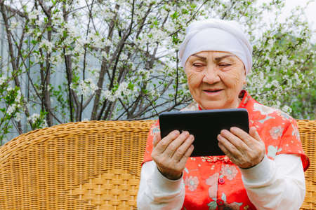 Portrait of a smiling Asian elderly woman watching into a tablet in her handsの写真素材