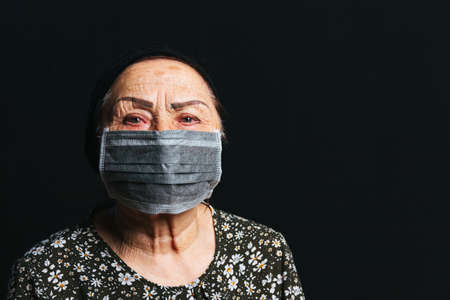 Portrait of an elderly woman in medical mask on a black background. Old people in risk zone because of virus epidemy, COVID-2019 pandemicの写真素材