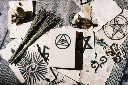 White magic book laying on the table with old manuscripts with occult symbols, candles, lavender. Concept of fortune telling, ritual, altar, spiritism, secret knowledgeの写真素材
