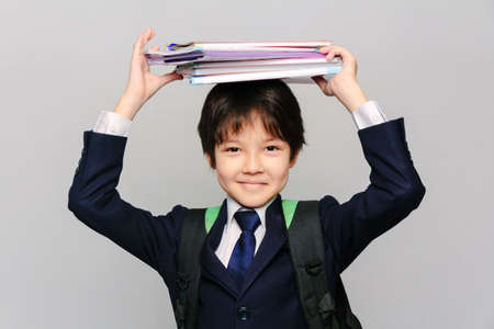 Close-up portrait of an Asian schoolboy holding his textbooks on his head and smilingの写真素材