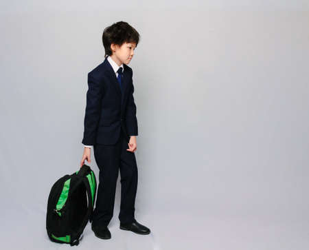 Portrait of an Asian schoolboy dragging his schoolbag behing him tired