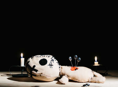 Pins with skulls stabbed in a voodoo doll for your magic ritual on a black background with candleの写真素材