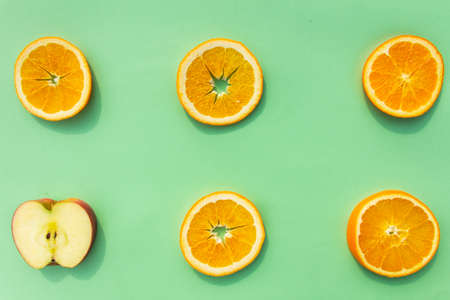 Bright, tasty, fresh, juicy orange slices with an apple slice on green background, natural vegan food, good for alphabet, vitamins for immune systemの写真素材
