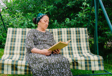 Portrait of an old Asian woman reading a book in her garden, thinkingの写真素材