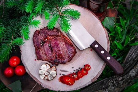 Pork steak with garlic, pepper and tomatoes on a board with a knife and herbsの写真素材