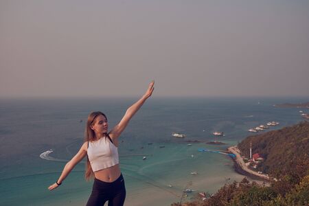 Girl model in shorts, swimsuit and T-shirt stands and sits on the rocks in the mountains against the sea and ocean, on a sandy beach in Thailandの写真素材