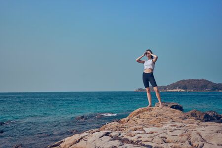 Girl model against the sea and ocean in peas and on stones in shorts and swimsuit in Thailandの写真素材