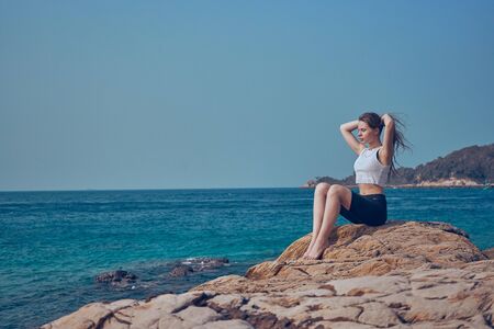 Girl model against the sea and ocean in peas and on stones in shorts and swimsuit in Thailandの写真素材