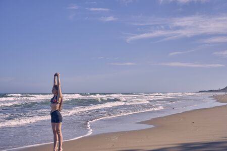Girl model against the sea and ocean in peas and on stones in shorts and swimsuit in Thailandの写真素材