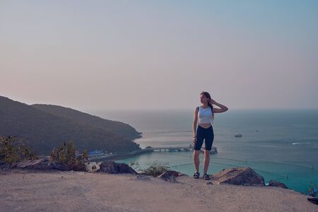 Girl model against the sea and ocean in peas and on stones in shorts and swimsuit in Thailandの写真素材