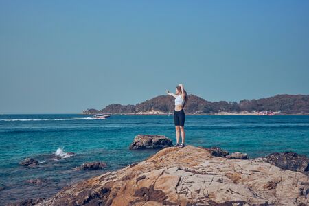 Girl model against the sea and ocean in peas and on stones in shorts and swimsuit in Thailandの写真素材