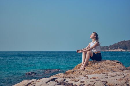 Girl model against the sea and ocean in peas and on stones in shorts and swimsuit in Thailandの写真素材