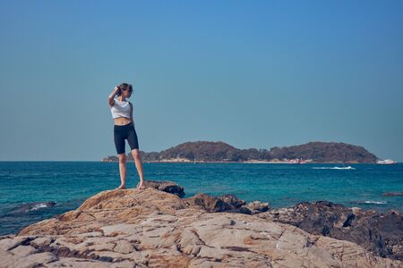 Girl model against the sea and ocean in peas and on stones in shorts and swimsuit in Thailandの写真素材