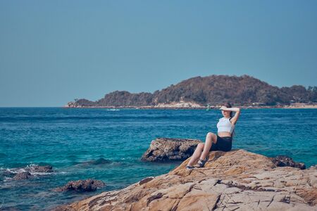 Girl model against the sea and ocean in peas and on stones in shorts and swimsuit in Thailandの写真素材