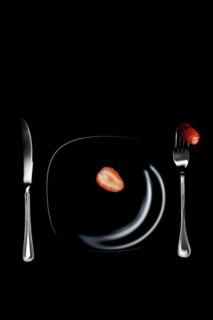 Fork, knife, plate with strawberries on a black tableの写真素材