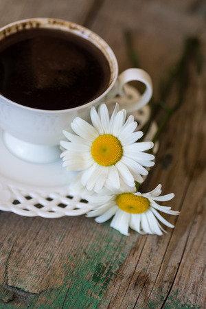 A cup of coffee and chamomile on a wooden tableの写真素材