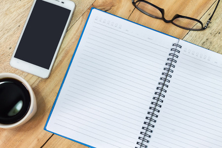 Office supplies, notebook, coffee, smartphone and pencil on wood desk.
