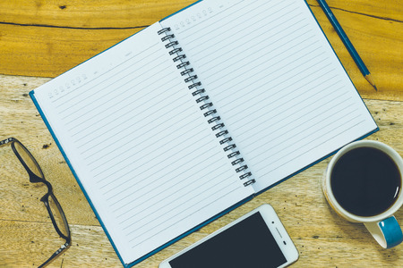 notebook, coffee, smartphone and pencil on wood desk.