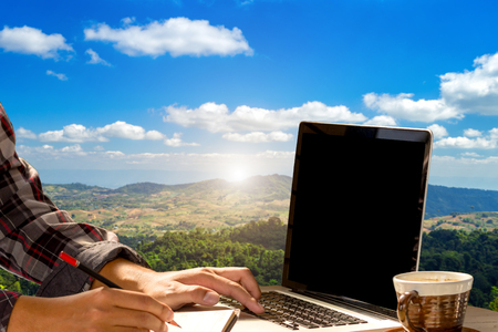 Businessman working with of laptop with blank white screen and coffee view mountain range on Blue sky background.の写真素材