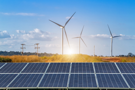 solar panels with wind turbines against mountanis landscape against blue sky with cloudsの写真素材