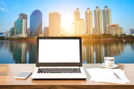Mockup image of laptop with blank white screen on wooden table view outdoors of office building cityscape background.の写真素材