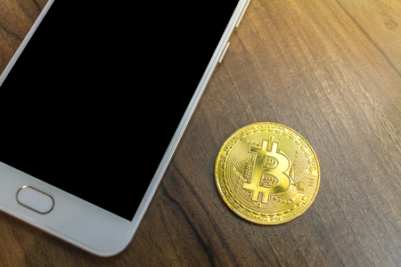 Bitcoin coin and smartphone on old wood desk on top.の写真素材