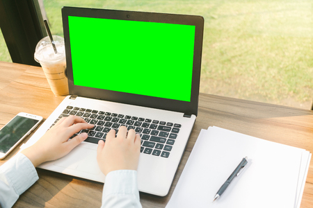 Close-up of business female working with laptop with blank green screen make a note document and smartphone in coffee shop like the background.の写真素材