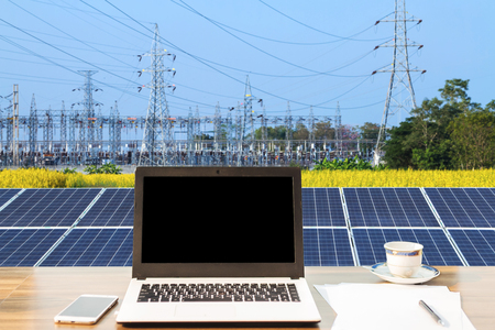 Mockup image of laptop with blank black screen,smartphone,coffee cup on wooden table of solar panel on high voltage tower in blue sky background, Alternative energy concept,Clean energy,Green energy.の写真素材