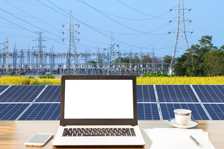 Mockup image of laptop with blank white screen,smartphone,coffee cup on wooden table of solar panel on high voltage tower in blue sky background, Alternative energy concept,Clean energy,Green energy.の写真素材