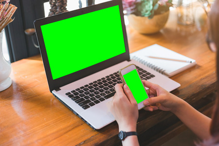 Close-up of business female working with smartphone with blank green screen make a note document and laptop with blank green screen in coffee shop like.の写真素材