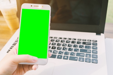 Close-up of business female working with smartphone with blank green screen make a note document and laptop in coffee shop like.の写真素材