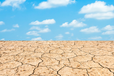 Brown dry soil or cracked ground texture on blue sky background texture with white clouds.の写真素材