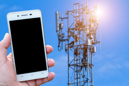 Men use smartphone blurred images in Antenna on communication or electricity tower radio mast with aerial antenna with blue sky background.の写真素材