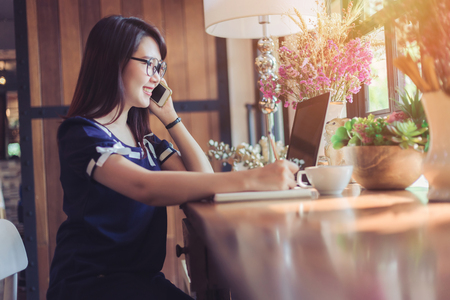 Business Asian woman hold pick up Smartphone working with laptop computer on in coffee shop like the backgroundの写真素材