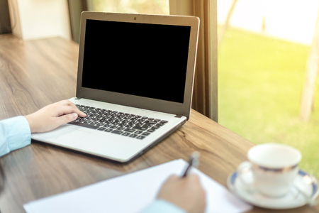 Close-up of business female working with laptop with blank white screen make a note document and smartphone in coffee shopの写真素材