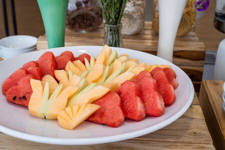Chop the pieces of watermelon and pineapple in white dish the dining and flower vase on table decorationat buffet self service at hotel.の写真素材