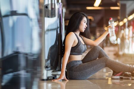 Fitness Asian women sitting in sport gym interior and fitness health club with a bottle of water.の写真素材