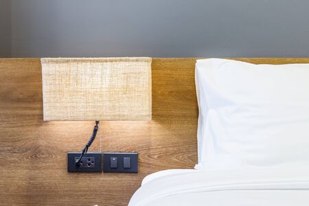 Close-up of white pillow on bed decoration with light lamp in hotel bedroom interior.の写真素材