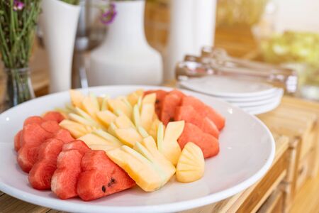 Chop the pieces of watermelon and pineapple in white dish the dining and flower vase on table decorationat buffet self service at hotel.の写真素材