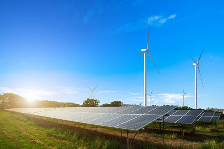 solar panels with wind turbines against mountains landscape against blue sky with clouds,...