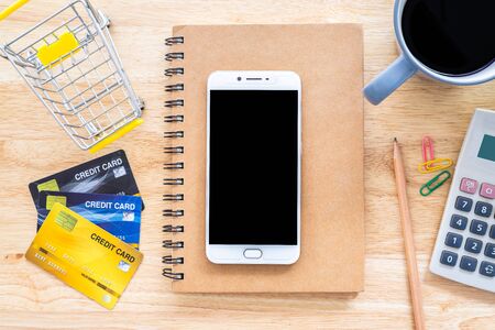 Credit cards,notebook,flower pot tree,smartphone,Shopping cart and coffee cup on wooden background,Online banking Concept,Top view office table.の写真素材