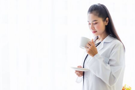 Portrait of asian young female doctor eating coffee from a cup and stethoscope with in hospital background.の写真素材